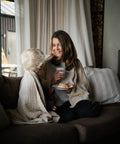 En kvinna i soffan med den beige muslinfilten Stora Sand